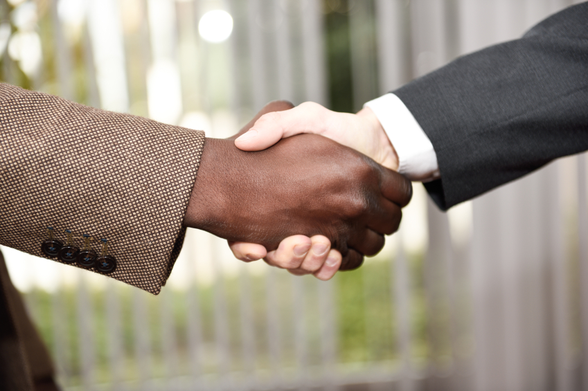 Black businessman shaking hands with a caucasian one wearing suit in a office. Close-up shot